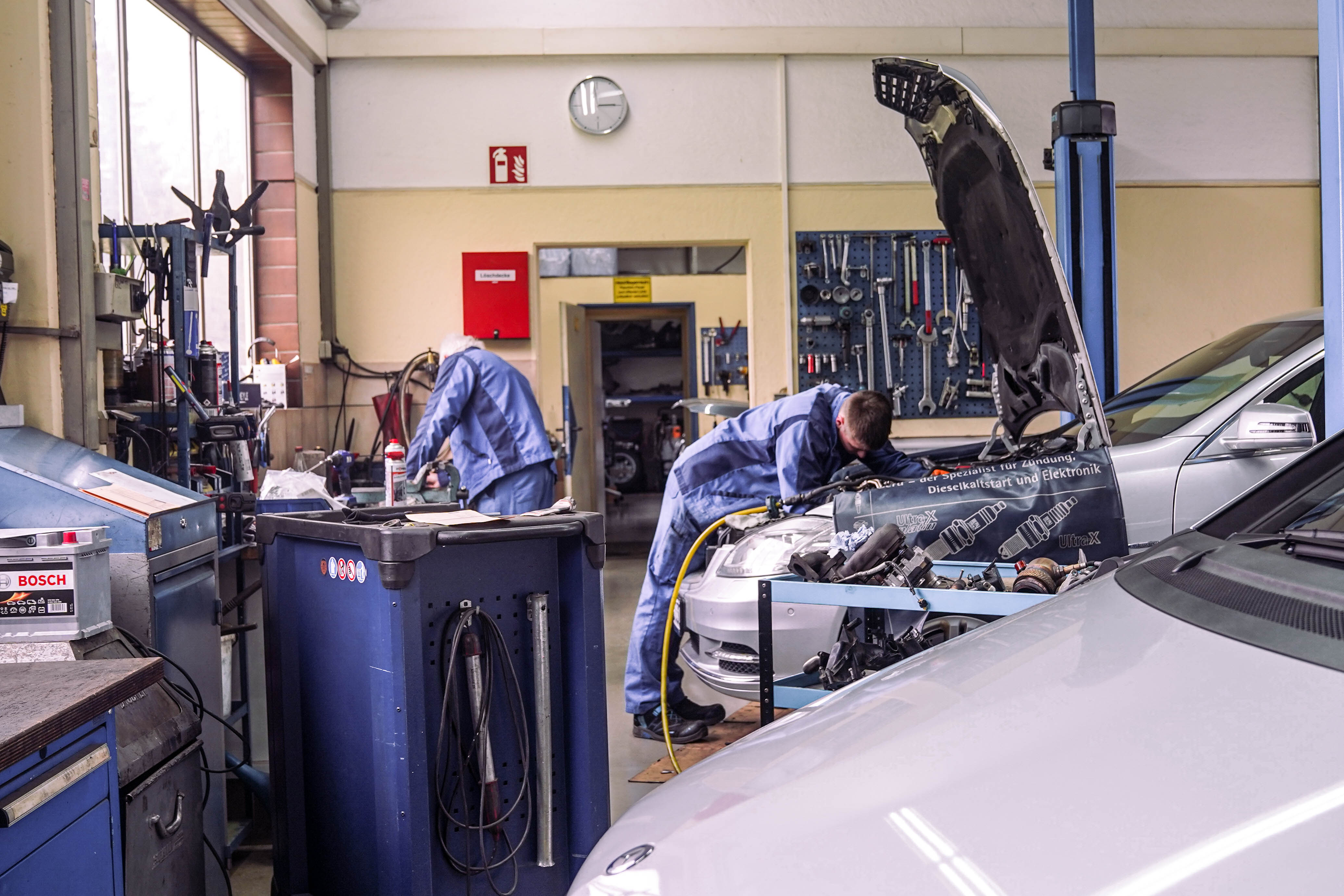 Blick in die Werkstatt mit zwei Mechatronikern an Fahrzeugen